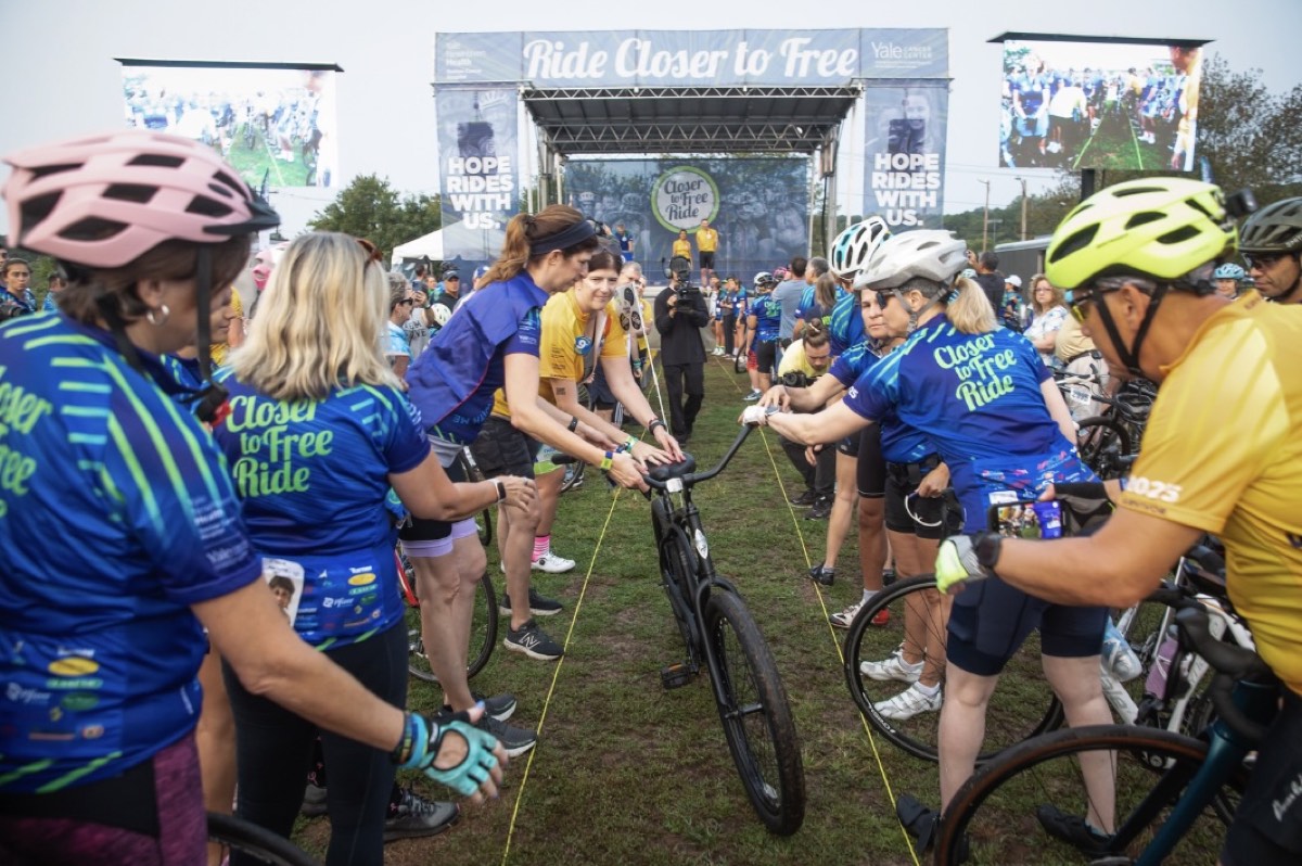 Riders passing a bicycle hand-to-hand under the Closer to Free Ride arch